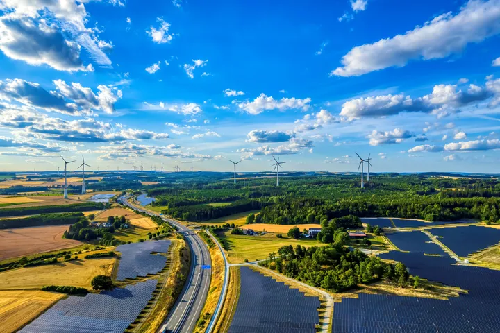 Regionale Erzeugung von erneuerbarer Energie Eine Luftaufnahme zeigt Windräder und Solarfelder in der Landschaft bei klarem Himmel.