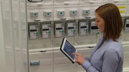 Intelligentes Messsystem iMSys Eine Frau steht mit einem Tablet in der Hand vor Zählern und tippt etwas in das Tablet