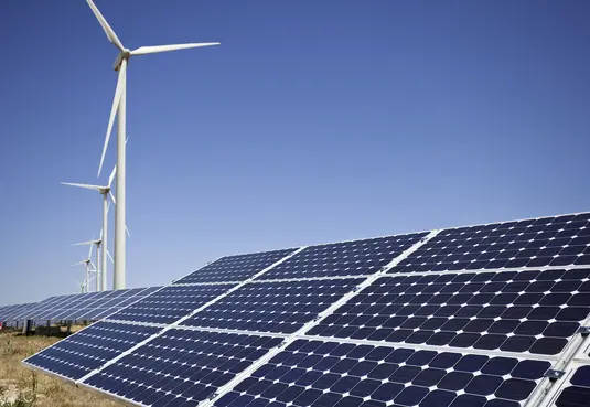 Photovoltaikanlage mit Windrädern im Hintergrund bei blauem Himmel