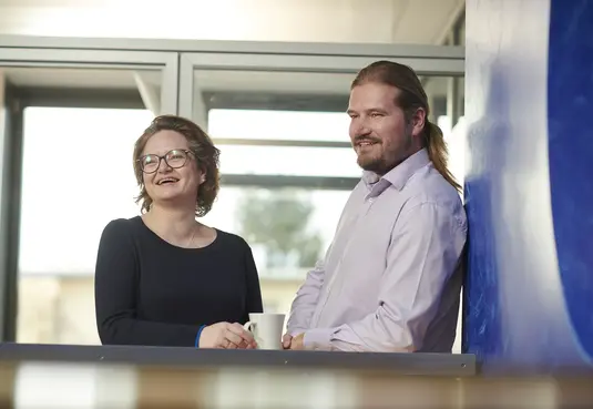 eine Frau und ein Mann stehend mit einer Tasse im Büro